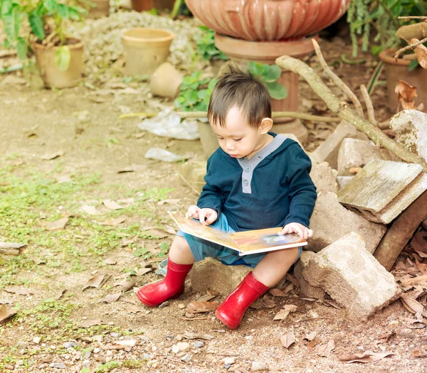Asiatischer Baby-Junge liest Märchenbuch, der Junge trägt rote Stiefel sittin — Stockfoto