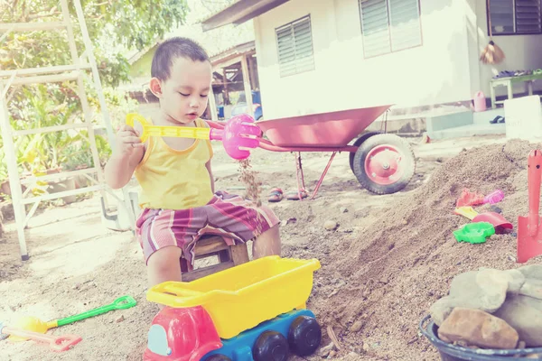 Thai baby boy palying on  pile of sand with toy and plastic fork, spoon , truck ,wheel barrow — Stock Photo, Image