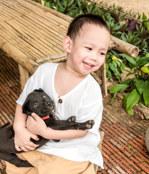 S úsměvem Asijské dítě chlapec objetí malé černé psí v ruce Stock Snímky