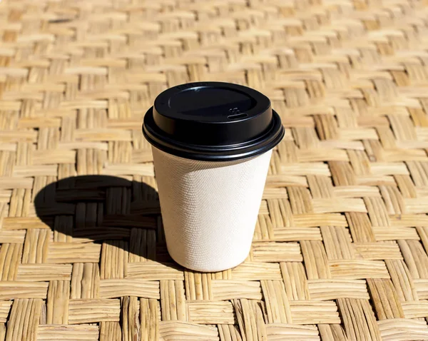 Бумажная чашка кофе положить на ротанга мат против утреннего света — стоковое фото