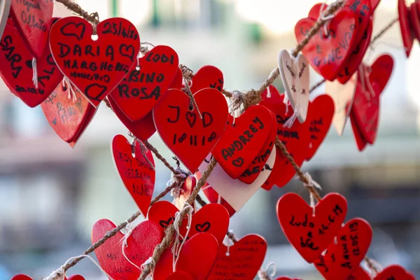 A large group of plastic red heart-shaped notes, with names written above, hanged as a love promise and love sign. They are utilized to show all over own love for a loved ones.