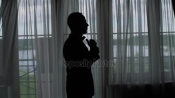 Man adjusts black bow tie silhouette backlit slow motion middle shot. Unrecognizable noble royal family member corrects straightens classic bowtie wears suit prepare for wedding or businessman go out — Stock Video