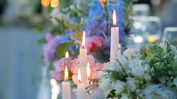 Velas e flores fechar colorido macro câmera lenta profundidade rasa de campo. Conjunto de mesa para banquete de recepção de casamento desfoque vidro de fundo. Longa chama vela de cera luz ambiente romântico acolhedor — Vídeo de Stock