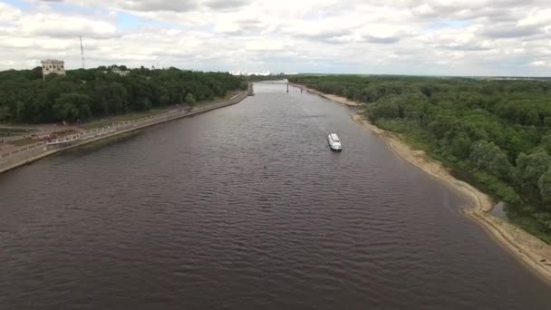 Voler au-dessus de la rivière à Gomel Biélorussie aérienne 4K HD. Drone haut au-dessus des eaux de Sozh avec bateau de croisière à moteur et remblai de la ville avec zone de bois vert vue touristique journée d'été par drone copter 