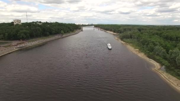 Полет над рекой в Гомеле Беларусь воздушный 4K HD. Беспилотник высоко над водами Сожа с круизным кораблем и городской набережной с зеленой лесной зоной — стоковое видео