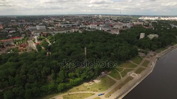 Gomel Belarús aérea 4K HD. Volar sobre los edificios de la ciudad y aparcar en el río Sozh con terraplén vista panorámica del paisaje superior. Crucero barco a motor se mueven en el agua y el área de madera verde banco del otro lado por dron — Vídeo de stock