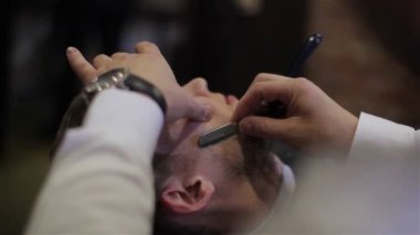 Adam olan kuaför dükkanında tıraş yakın çekim. Profesyonel Kuaför Saç kesmek için jilet gibi keskin bıçak ve krem jel ile kullanarak müşteri yüzüne bıyık, kıllar. Mutlu gülümseyerek berber istemci memnun
