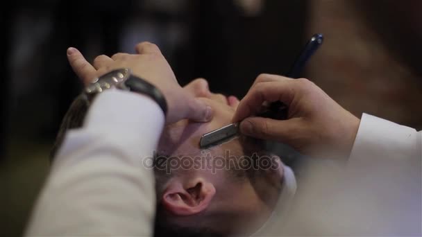 Un hombre afeitándose en la peluquería de cerca. Peluquero profesional que utiliza afeitadora con cuchilla afilada y gel de crema para cortar cerdas de pelo de bigotes en la cara del cliente. Feliz sonriente cliente de barbería satisfecho — Vídeo de stock