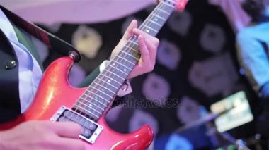 Ağır çekim oyun gitar yakın. Erkek el parmaklarında notları yeni kırmızı elektro gitar parlayan fretboard üzerinde tutarak akorları basın. Gitarist canlı konser kulüpte gerçekleştirir. Rock yıldız solo fotoğraf yanıp söner