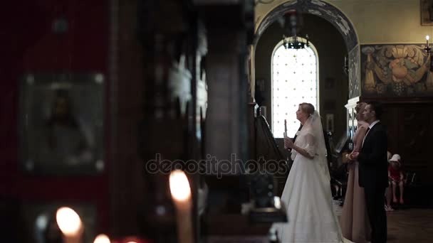 Bride and groom stand with candle at wedding ceremony in orthodox church in Nice France. Best man and maid of honor bless crossing behind betrothed. Greek orthodox church ritual traditions and customs — Stock Video