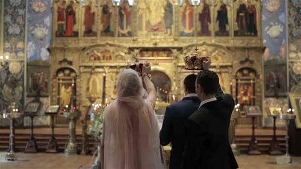 ギリシャ正教の教会の儀式の伝統や習慣。Koumbaro 最高の男と花嫁介添人と素敵なフランスの正教会式の祭壇の前で司祭によって祝福されたカップルの結婚の上の冠を保持します。 — ストック動画