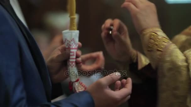 Sacerdote ortodoxo realizando rito de intercambio de anillos para casarse pareja novia y novio en la ceremonia de la boda en manos de la iglesia dedos de cerca. Ropa ceremonial vestimenta dorada en la tradición ortodoxa — Vídeos de Stock