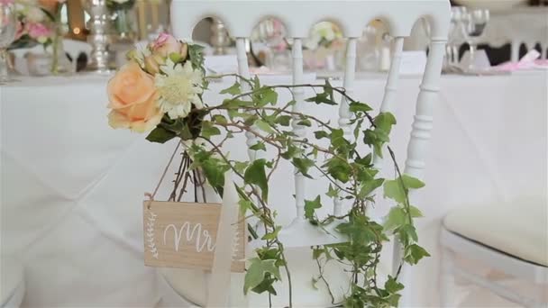 Green wedding decor on chair for reception close up. Flower bouquet and wild ivy twigs used as decoration at white chair arranged in guest seat area. Wedding plan florist work floral elements decision — Stock Video