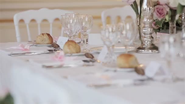 Decoración de la vajilla disposición de la mesa festiva cerca de cambiar detalles de enfoque rack. Mesa de recepción de boda con tarjetas de lugar de invitados con vasos cubiertos flores y bollos de pan en platos listos — Vídeos de Stock