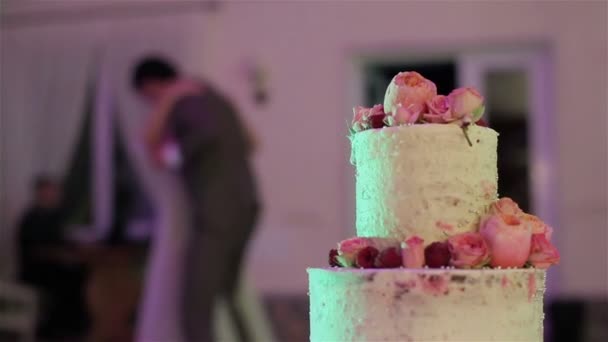 Hombre y mujer bailando en el fondo de la hermosa tarta de boda decorada con rosas naturales florece y bayas de cerca. Recepción de banquetes y catering. Decoración floral en cocina — Vídeos de Stock
