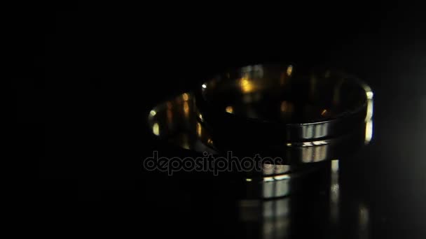 Anéis de casamento fundo preto brilhando com luz jóias fechar macro. Dois noivo noiva e anéis de glamour par deitado na superfície escura iluminado a partir de cima com mudança espelho reflexão iluminada — Vídeo de Stock