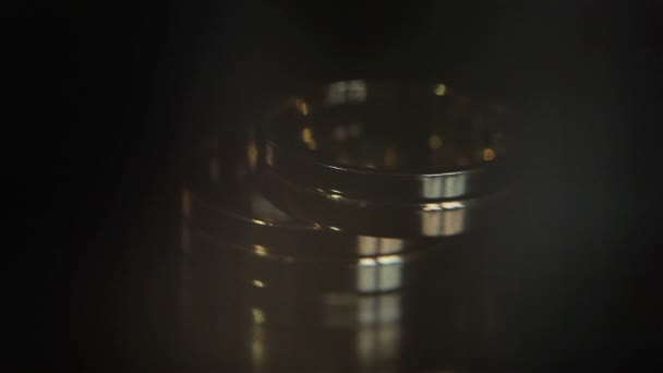 Trouwringen zwarte achtergrond schijnt met lichte sieraden dicht macro. Twee bruid en bruidegom glamour ringen paar liggend op donkere oppervlakte omhoog van verlicht top met de spiegel reflectie verlicht wijzigen — Stockvideo