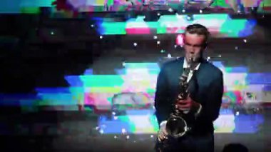 Yeni yıl partisi saksafon gece kulübünde oynarken adam. Onun saz ve klik ve arıza vj ekran projeksiyon arka plan yakın çekim parmak dayama yakışıklı karizmatik sanatçısı