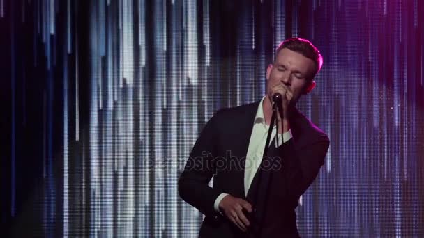 Man sings with mic on night club concert stage close up. Stylish charismatic singer performs song jazz soul emotionally at light LED screen background with abstract animation of slow moving waterfall — Stock Video