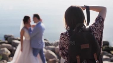 Düğün fotoğrafçısı tanınmayan yeni evli gelin ve damat çift açık havada deniz ve arkadan aydınlatmalı güneş arka plan poz verme fotoğraf çalışır. Düğün fotoğrafçılığı ve aşk hikayeleri videografisi