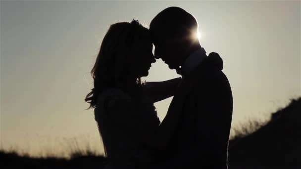 Paar omhelzing afsteekt bij zonsondergang sluwe achtergrond close-up. Man en vrouw contrast schaduw pose buitenshuis permanent samen onder gouden uur zon ray balken schijnt. Afscheid tederheid relatie — Stockvideo