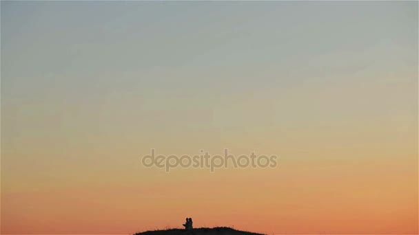 Homme étreint femme debout sur le sommet de la colline avec beaucoup de ciel vu loin au coucher du soleil ciel fond plan large. Homme prenant des photos avec smartphone de vue de la montagne pendant les vacances de lune de miel — Video