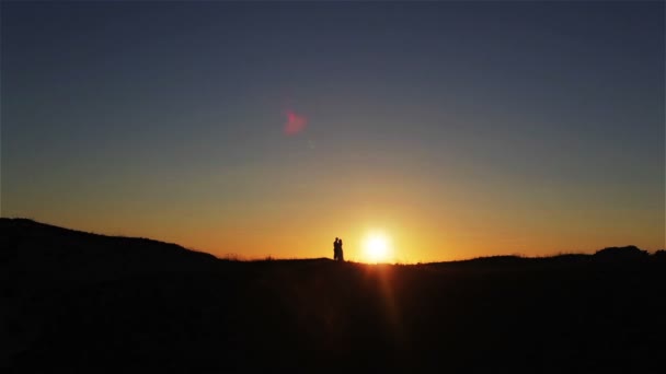 Mann und Frau stehen umarmt am Himmel bei Sonnenuntergang. Verliebte Paare küssen sich auf einem Hügel im Freien. Liebe Einheit Miteinander Beziehungskonzept — Stockvideo