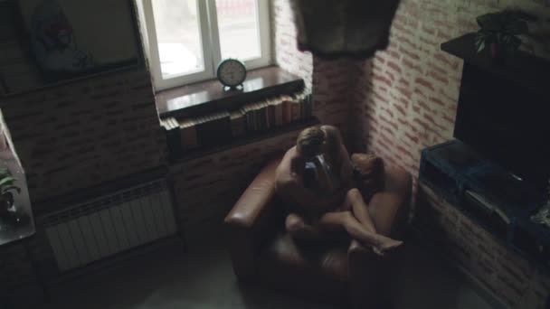 Пара влюбленных поцелуев в помещении, сидящих в кресле с видом сверху. Молодой человек и женщина обнимаются дома, обнимая друг друга крепко. Интимный момент близости друг с другом — стоковое видео