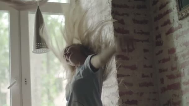 Mulher dança pulando em casa pela janela lançando o cabelo e sorrindo enquanto o homem observando-a pacientemente sentado no peitoril da janela câmera lenta. Menina loira bonita se divertir relaxante no fim de semana — Vídeo de Stock