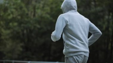 Adam sabah yavaş hareket yok yüzünü yakın dağ ormanda koşu. Erkek koşucu yan arka görünüm kapşonlu gri kazak ve eğitim pantolon tepeye çalıştırmak. Sağlık egzersiz açık hava yaşam tarzı