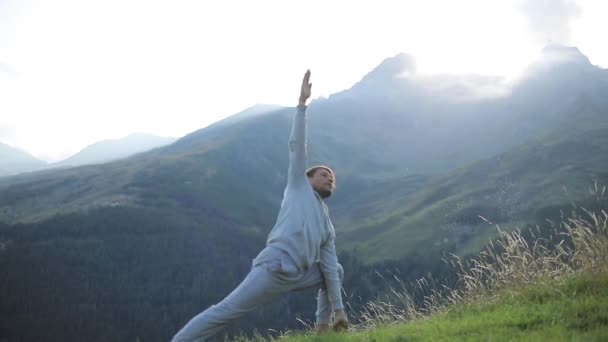 男人的瑜伽体式站搁置抬头慢动作的高山草甸。行使在自然与阳光照耀出峰值的锻炼姿势。为培训强壮的身体在户外日常男运动服 — 图库视频影像