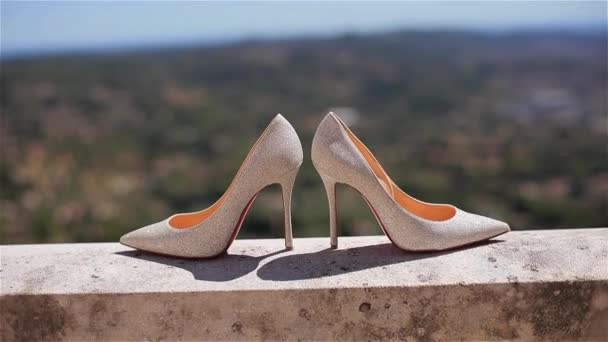Женская обувь закрывает лубутены на зеленом летнем пейзаже мелководья. Красивая пара стильных роскошных невесты на высоком каблуке белый шпилька из материала, сияющий отражающий солнце стоять на балконе или террасе — стоковое видео