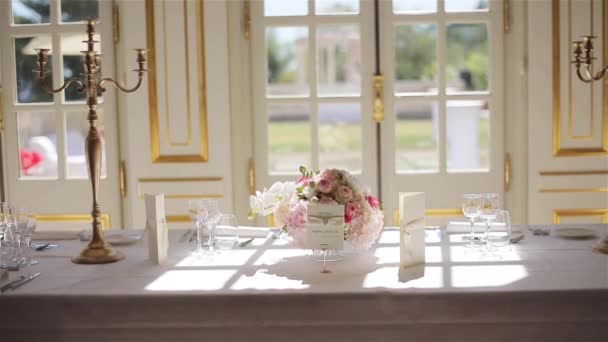 Feestelijke tabel ingesteld met glazen en bloemen boeket bij zon licht dicht. Elegante serviesgoed met kandelaar gerangschikt voor diner of lunch eten in restaurant. Fine dining bruiloft receptie catering — Stockvideo