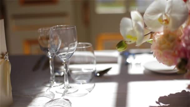 Menükarte leere Gläser für Weinwasser und rosa Blütenstrauß auf weißer Tischdecke arrangiert für feines Essen Verfolgung Makro Nahaufnahme. festlich eleganter Tisch zum Essen im Restaurant Café Bankett gedeckt — Stockvideo