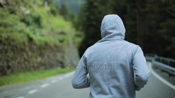 ジョギング山道顔戻っては男は、スローモーションを閉じません。朝のグレーのフード付きセーターの屋外だけでランナー。自然の中のスポーツ男を実行するスプリント運動およびトレーニング。自由と選択 — ストック動画