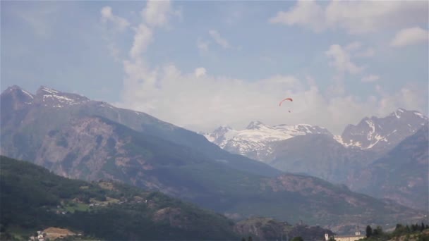 滑翔伞在山风景远的距离 一只滑翔伞飞行使用橙色伞漂浮下来盘旋慢低在树太阳雪山顶夏天录影看法谷 航空体育旅游 — 图库视频影像