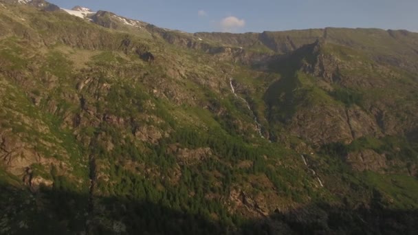 Zelená Hora hill s malými dlouhý vodopád a lesní stromy rostoucí na svahu letecké 4k. Pomalý Přelet nad prosluněné Alpy hřeben s pramenité vody z pohledu zasněžené nejlepší letní večer. Čistý vzduch — Stock video