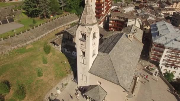 4 k παλιά αρχαία εκκλησία καμπαναριό διοδίων για Κυριακή μάζα ανθρώπων που περιμένουν να υπεισέλθω. Εναέρια από ψηλά τη θέα πάνω από την μικρή ιταλική πόλη Κουρμαγιέρ κεραμιδιών στέγες κοιλάδα της Αόστα, στους πρόποδες του Mont Blanc βουνό — Αρχείο Βίντεο