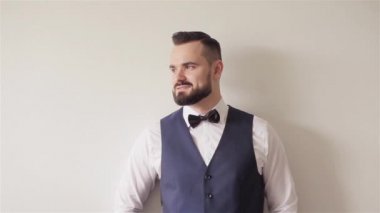 30'lu portresi kamera gülümseyen beyaz duvara poz standları görünüyor papyon adamla sakallı. Genellikle kuaför dükkanı istemci saçlı. Görünüm giyim kıyafetleri aksesuarları ve klasik erkek moda ayrıntıları