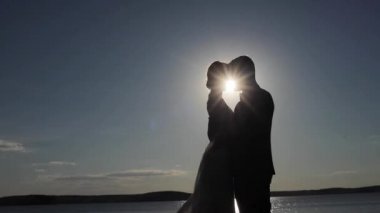 Kontrast çift aşık kucaklamak ve samimi an birlikte gökyüzü arka plan kontrast gölge akşam güneş Parlatıcı ışık ışınları tadını çıkarın. Adam kadını arkadan aydınlatmalı basılı kopya alanı birbirlerine öpücük. Aşık mümin