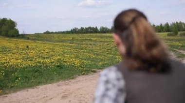 Karahindiba alan sarı doğal arka plan ağır çekim ile şenlikli giysili kız gelin sonra çalışan adam damat. Genç erkek yetişme kadın panoramik görünüm açık havada kopya alanı moda takip