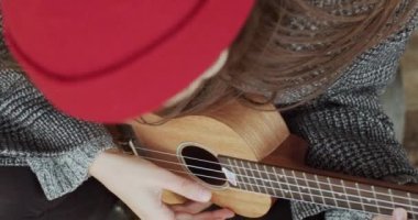 Ukulele çalan tanınmayan kızın yukarıdan görünüşü. Açık havada yavaş çekimde yakın çekim. Hawaii gitaristinin gitar enstrümanını tutan kadın eller makro detay çalıyorlar. Müzik mağazası