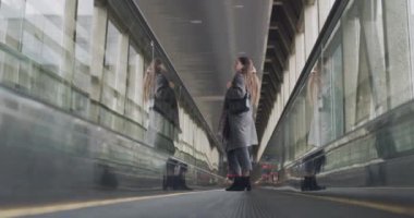 Demiryolu yürüyen merdiveninde duran genç ve güzel bir kadın ağır çekimde yana bakıyor. Uzun saçlı esmer kız tren istasyonunda naklediliyor. Seyahat turizm mimarisi