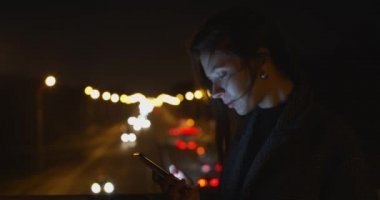 Yavaş çekimde akıllı telefondan mesaj gönderen bir kızın doğal portresi. Trafiğin parlak arka planında cep telefonu arayan genç bir kadının yan portresi. İletişim konsepti