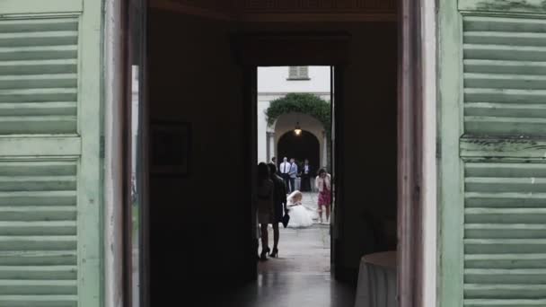 Door framed video portrait of bride in white dress sitting holding small dog on knees outdoors. — Stock Video