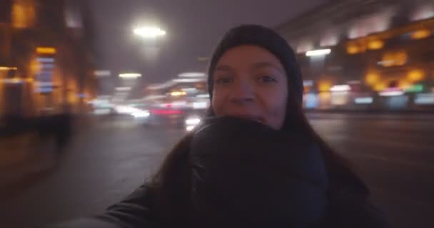 快乐的年轻女子手拿着相机 戴着冬衣帽 四处打转 女孩在城市夜景背景下旋转的自画像 幸福生活科技时尚 — 图库视频影像