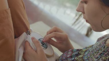 Beyaz kumaş dantel çerçeve kenarına göz nakışı yapan bir kadın. Yakın plan. Makro kız elinde iğne nakışı ile açık havada doğal hafif ağır çekimde. Hobi tekniği ekipmanı