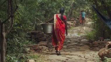 TIRUVANNAMALAI, Hindistan 1 Şubat 2020: Orman yolunda ağır yük taşıyan geleneksel giysiler içindeki Hintli kadının arka görünüşü. Sari 'deki kız yakacak odunları olan metal bir leğen tutuyor.