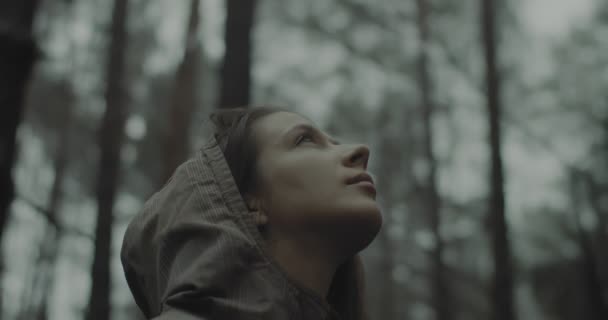 Κοντινό πλάνο πορτρέτο της νεαρής κοπέλας στέκεται στο δάσος και να ακούσετε τα πουλιά και τη φύση γύρω. Όμορφη γυναίκα που σκέφτεται, κοιτάζει ψηλά στον ουρανό και προσεύχεται το βράδυ. Ενότητα με τη φύση και την ευτυχία — Αρχείο Βίντεο