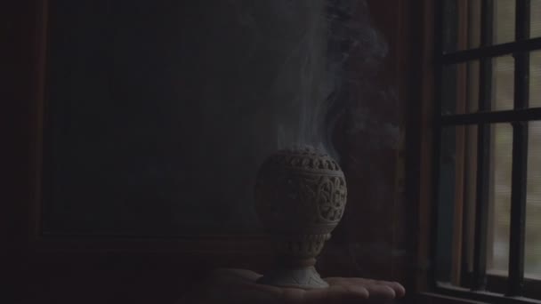 Faceless hand holding incense censer in darkness indoors copy text space. White smoke fume waving burning on black background slow motion close up. Indian fragrance sticks religion — Stock Video